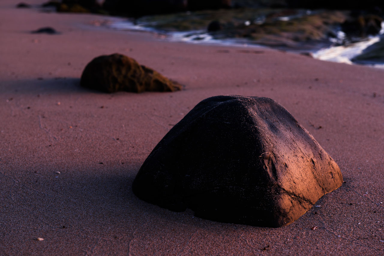 日没の光に照らされる砂浜の岩 Rocks on the beach illuminated by the light of sunset