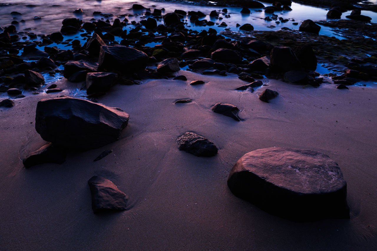 日没の光に照らされる砂浜と岩 Rocks and the beach illuminated by the light of sunset