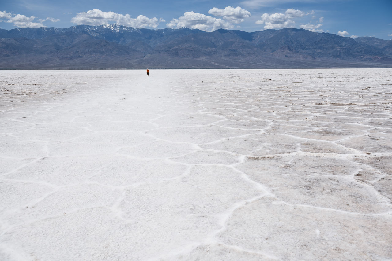 塩が一面に広がる日中のデスバレーの景色。遠方に人が一人歩いている。A view of Death Valley during the day with salt all around. One person is walking in the distance.